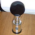 A black hockey puck proudly displayed atop a miniature Stanley Cup trophy.