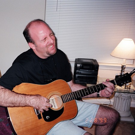 Jim playing the guitar in his bachelor pad apartment.