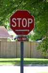 Stop sign with grafitti indicating 'Stop Consuming'.